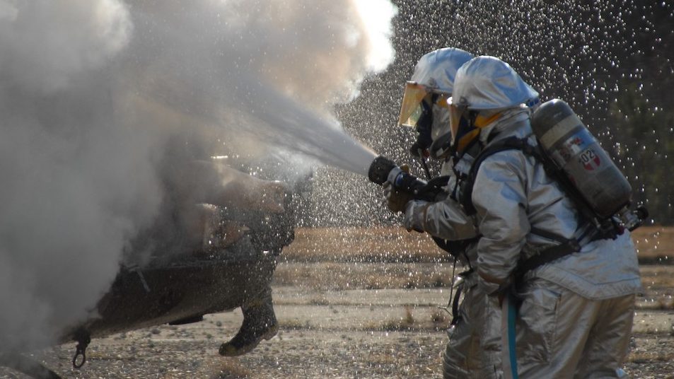 Two Firefighters train to extinguish aircraft fires while spraying foam from large hose