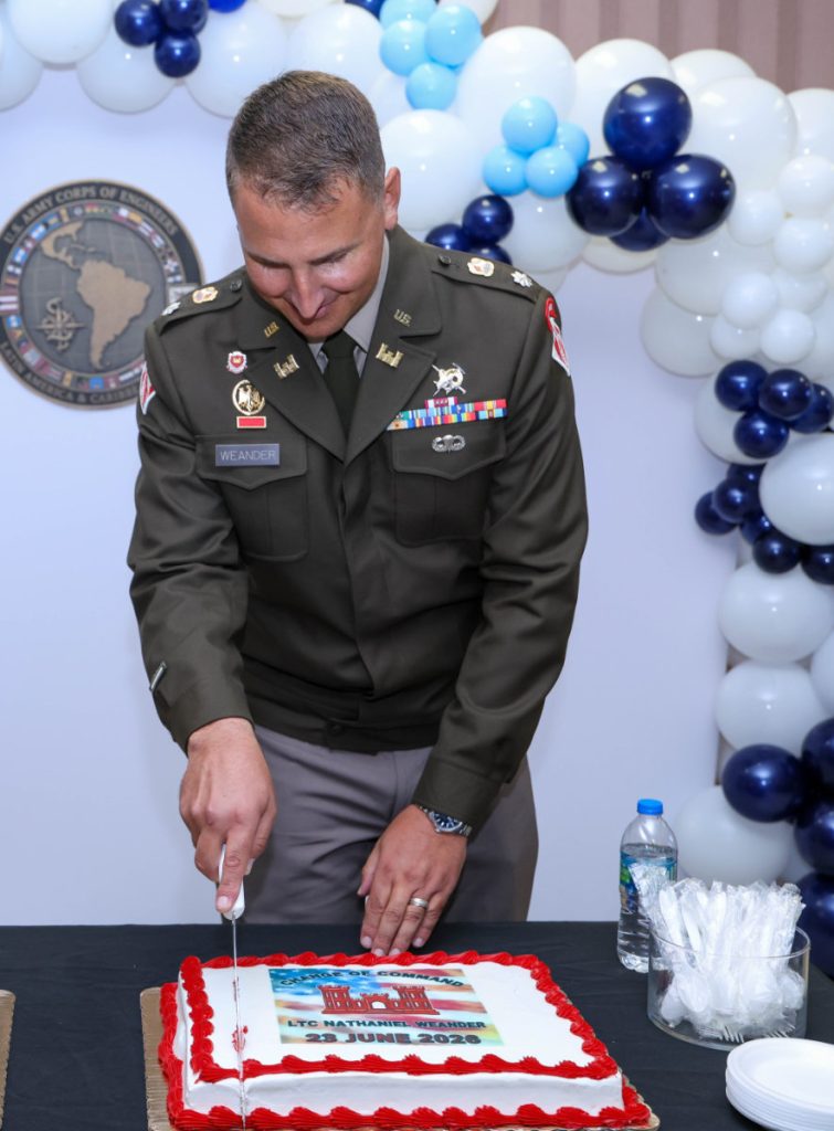An Army officer uses a knife to cut a ceremonial sheet cake decorated with the U.S. Army Corps of Engineers castle logo and a change of command inscription.
