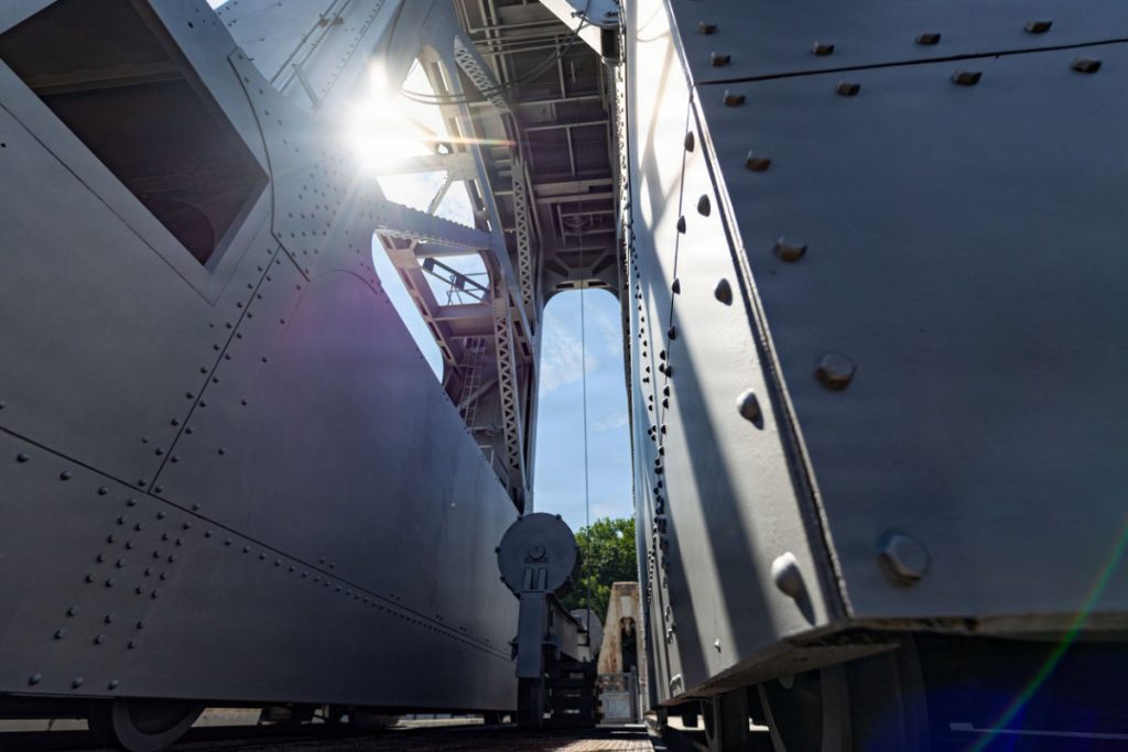 Sunlight glints through the steel framework of a freshly painted, grey gantry crane on top of a dam wall.