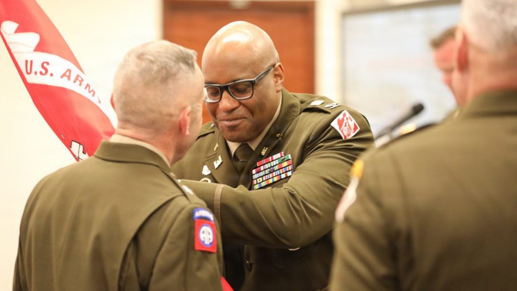 Close-up of Col. Marlon Ringo accepting the red unit flag from a general officer during a military change of command ceremony.