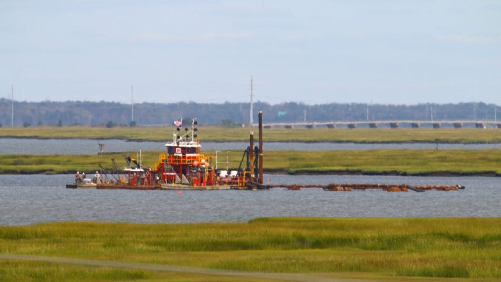 The Dredge Fullerton operated by Barnegat Bay Dredging Company sitting in a marshland channel with pipelines floating in the water nearby.