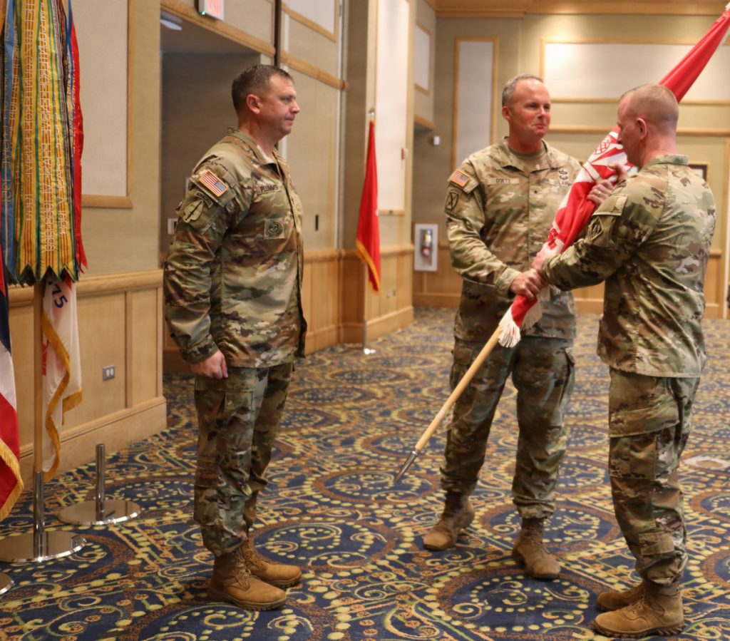 Army officers in operational camouflage uniforms execute the traditional passing of the red USACE flag during a change of command ceremony.