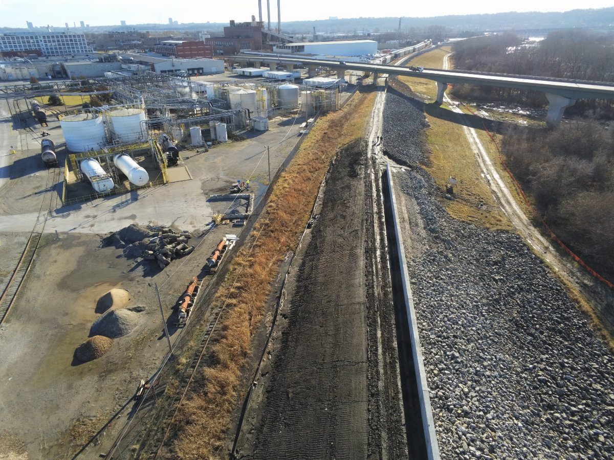 A newly constructed vertical concrete floodwall section stretching through an industrial corridor.
