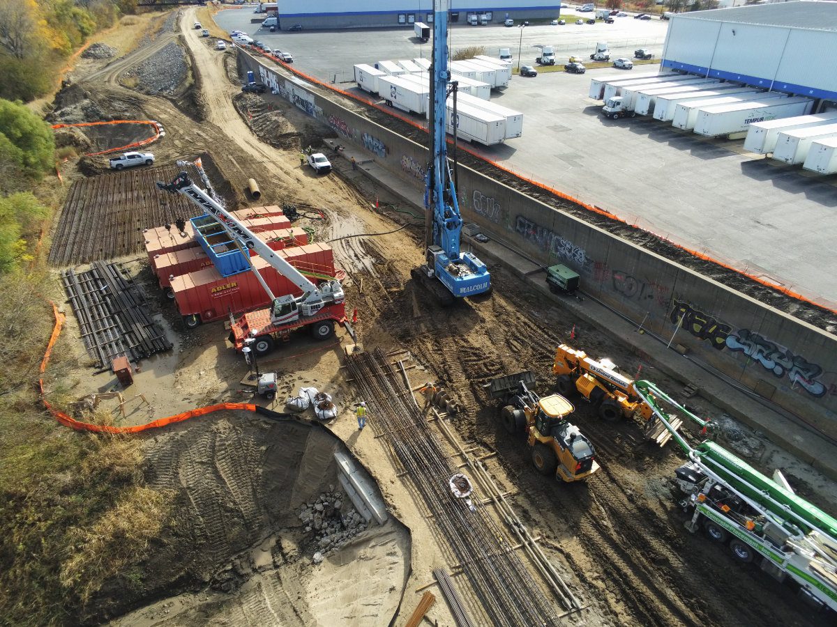 Heavy drilling rigs and earthmoving equipment preparing foundation shafts for levee expansion.