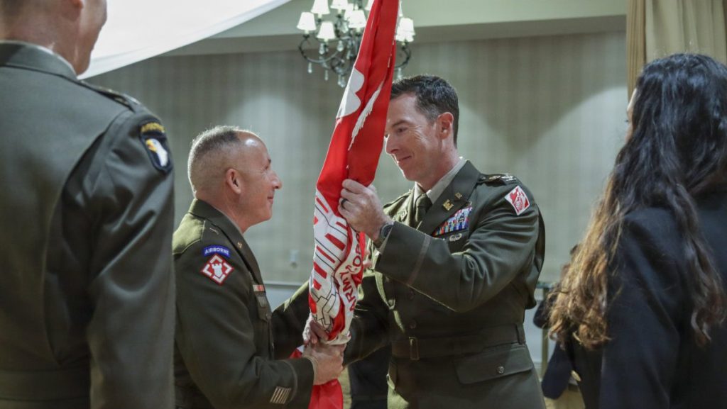 Col. Joshua Bost holds and accepts the red USACE organizational flag from a senior military officer during a passing of the colors ceremony.